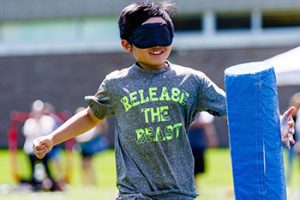 A blindfolded youth player runs to tag a padded base structure.